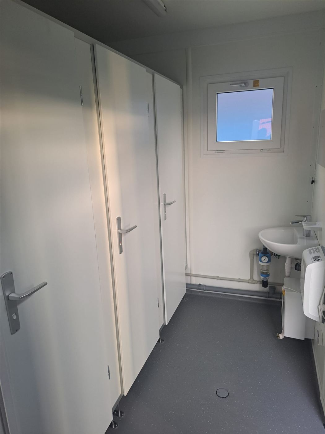 Kabinentüren im Sanitärcontainer und Waschbecken am Fenster