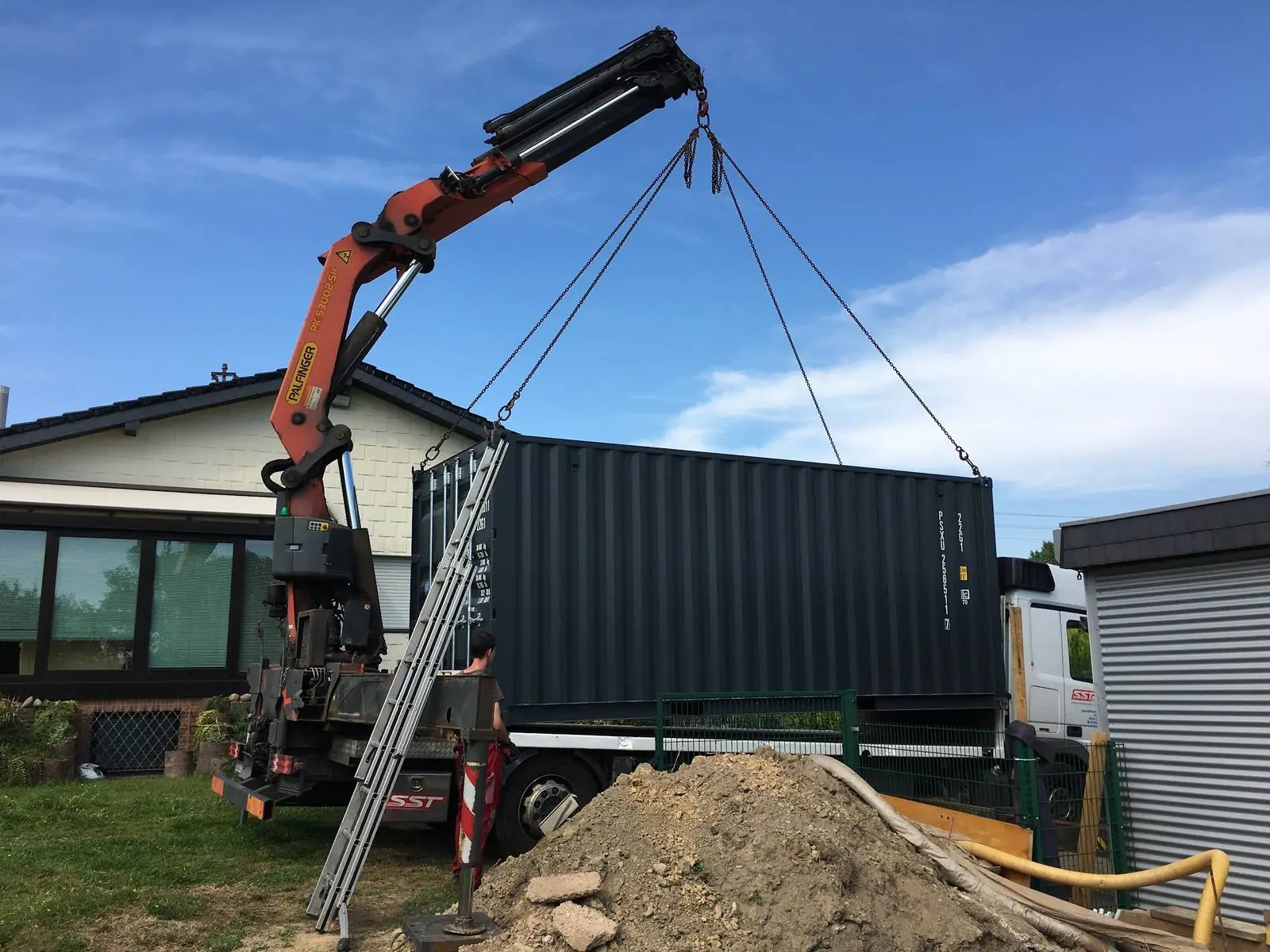 Seecontainer wird per Ladekran im Garten neben einem Wohnhaus abgesetzt